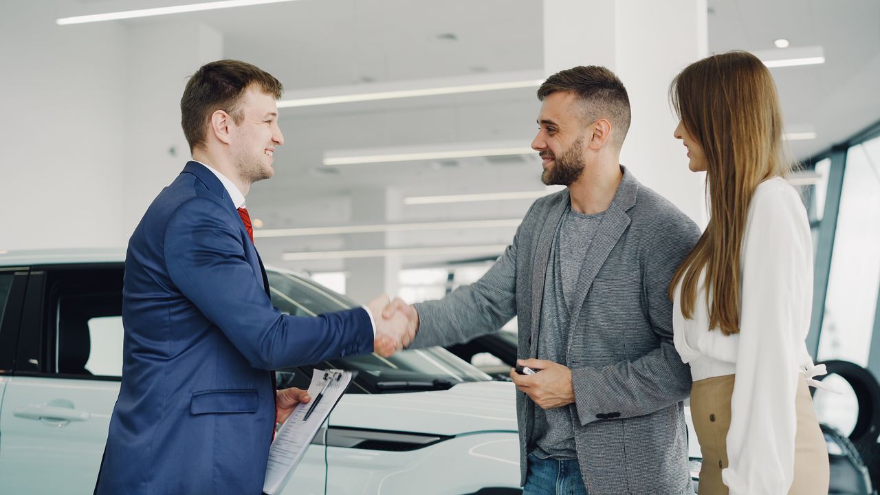 Friendly handshake between a car salesman and customers in a modern car showroom.