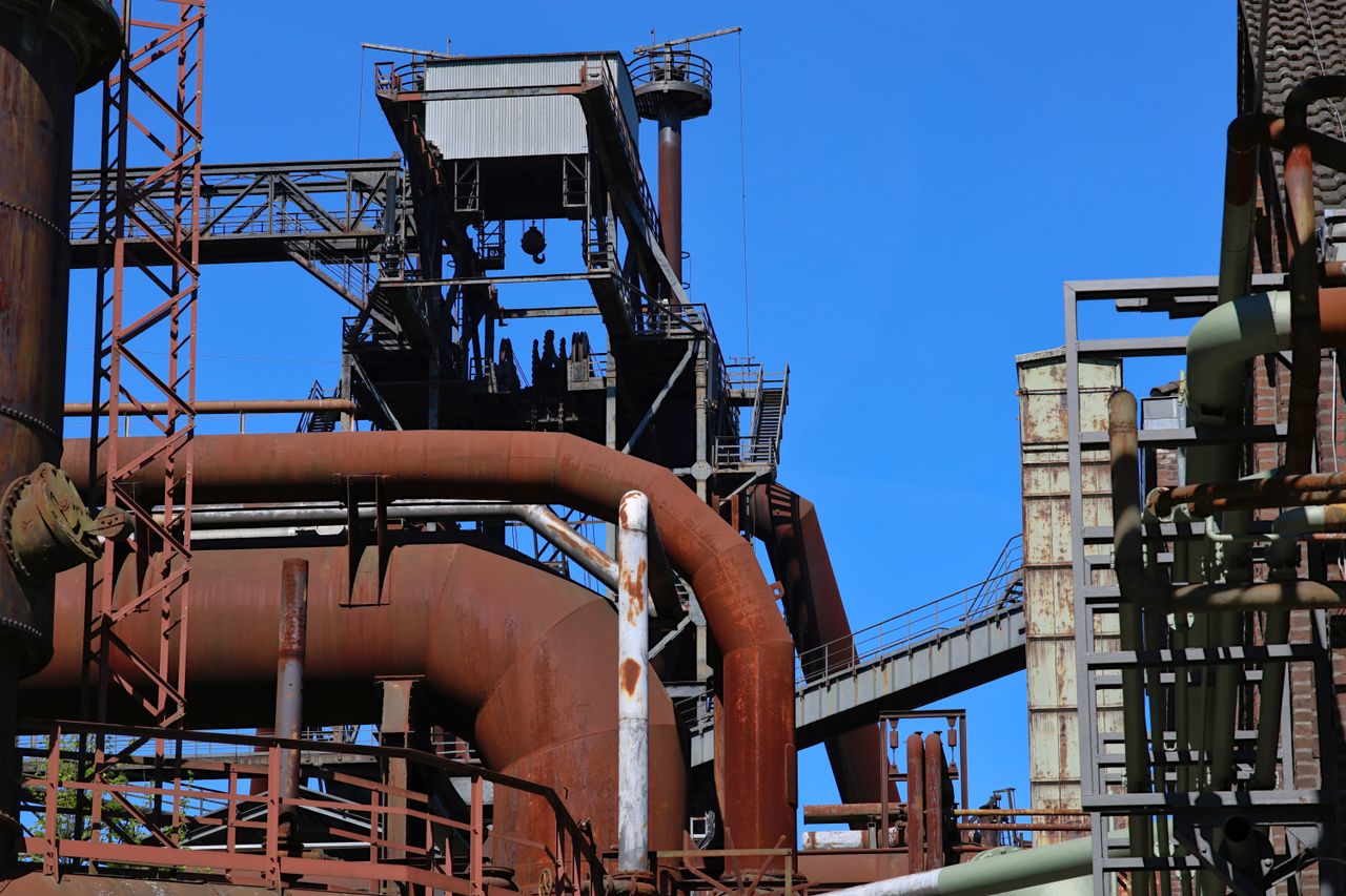 Detailed view of an industrial complex featuring rusted steel pipes and structures under a clear blue sky.
